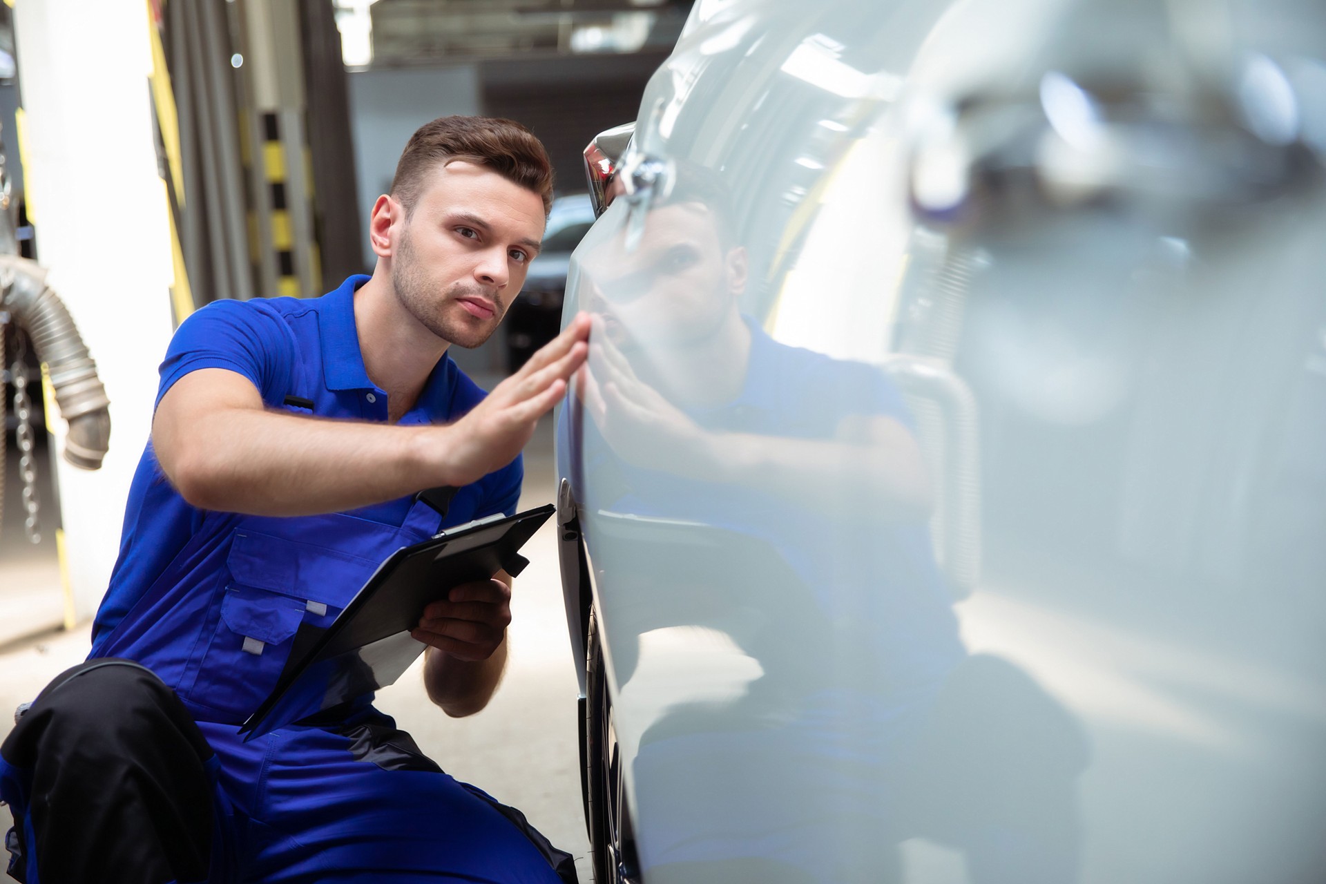 Confident and concentrated young and experienced car repair specialist with a tablet in his hand inspects and diagnosis the car for breakdowns